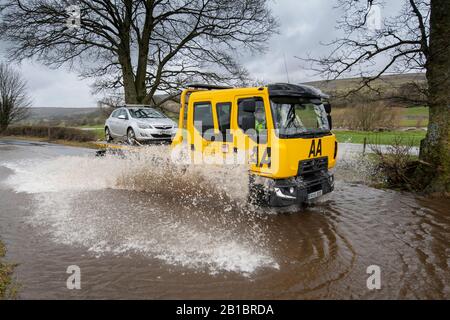 AA furgone di recupero con una macchina in corso attraverso inondazioni sulla A684 tra Hawes e Aysgarth a Wensleydale, North Yorkshire, UK. Foto Stock