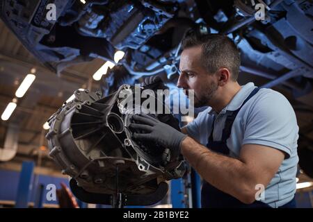 Drammatico ritratto a basso angolo di meccanica muscolare auto ispezione parte di auto in auto riparazione negozio, copia spazio Foto Stock