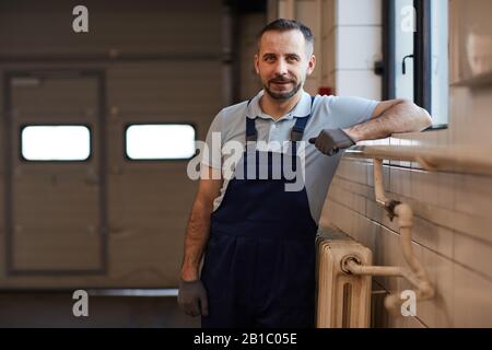 Girovita ritratto di macchina matura meccanico appoggiato a parete mentre posa in officina riparazione auto, copia spazio Foto Stock