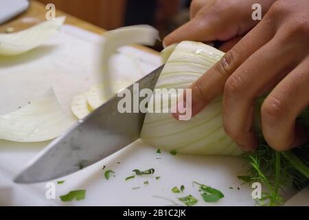 Mani che tagliano il finocchio su un tagliere con un coltello Foto Stock