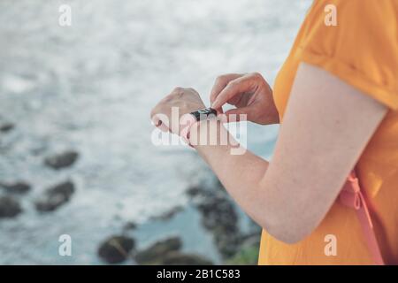 Donna escursionista utilizzando smart bracciale durante il trekking in natura. Close up di mani femminili portatile con dispositivo di informazione messa a fuoco selettiva. Foto Stock