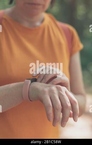 Donna escursionista che utilizza un braccialetto smart fitness tracker durante il trekking in natura. Primo piano di mani femminili con orologio fitness, fuoco selettivo. Foto Stock