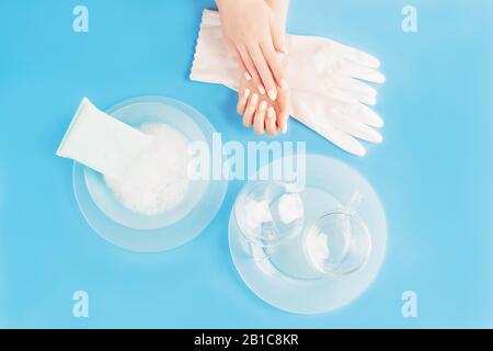 Piatti di lavaggio di concetto di fondo. Mani femminili con guanti di colore bianco perla, spugna per pulizia e bolle di sapone, belle lastre e bicchieri di vetro blu chiaro Foto Stock