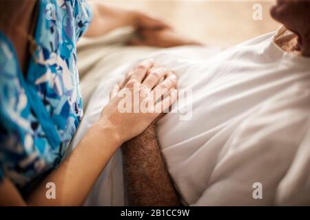 L'infermiere domestico giovane amichevole di riposo posa delicatamente la sua mano sopra la mano del paziente. Foto Stock