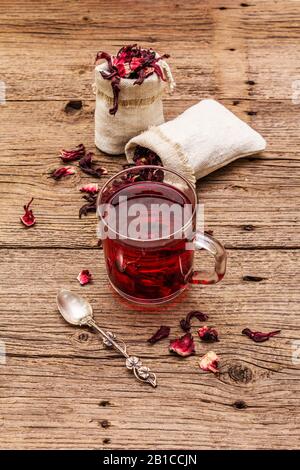 Tè hibiscus caldo. Petali asciutti, sacchi di lino. Cibo sano e concetto di auto-cura. Vecchi sfondi di tavole di legno, primo piano Foto Stock