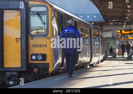 Arriva il convoglio ferroviario Nord accanto ad un treno di classe 150 a bordo della stazione ferroviaria di Sheffield con il logo arriva Northern sulla sua giacca Foto Stock