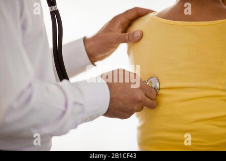 Mano di un medico che tiene uno stetoscopio contro la parte posteriore di un paziente femminile. Foto Stock