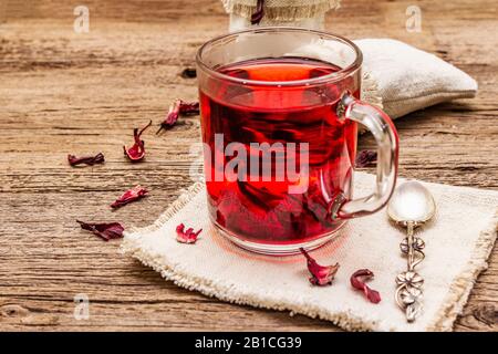 Tè hibiscus caldo. Petali asciutti, sacchi di lino. Cibo sano e concetto di auto-cura. Vecchi sfondi di tavole di legno, primo piano Foto Stock