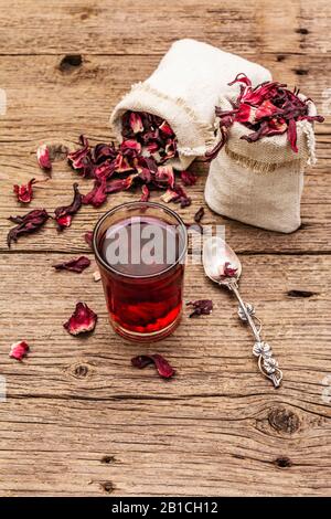 Tè hibiscus caldo. Petali asciutti, sacchi di lino. Cibo sano e concetto di auto-cura. Vecchi sfondi legno tavole, copia spazio, primo piano Foto Stock