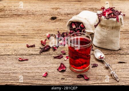 Tè hibiscus caldo. Petali asciutti, sacchi di lino. Cibo sano e concetto di auto-cura. Vecchi sfondi legno tavole, copia spazio, primo piano Foto Stock