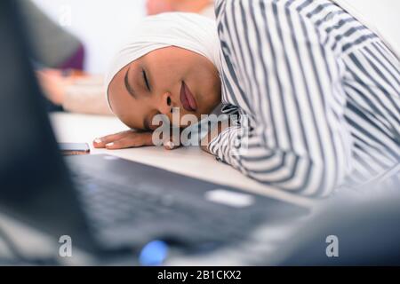 Donna musulmana africana di affari seduta alla sua scrivania e dormire isolato su sfondo bianco Foto Stock