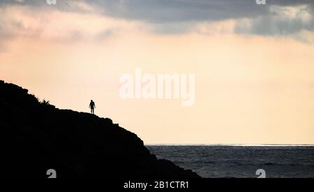 Vista mozzafiato della silhouette di un uomo non identificato che si erge su una scogliera che gode il tramonto. Mawi Beach, Bali, Indonesia. Foto Stock