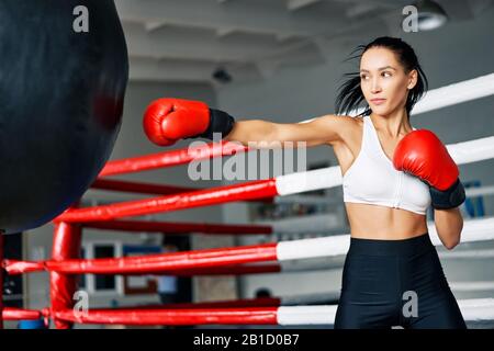 Pugile femminile che colpisce un enorme sacchetto di punzonatura in palestra fitness. Donna che pratica i suoi pugni in uno studio di boxe Foto Stock