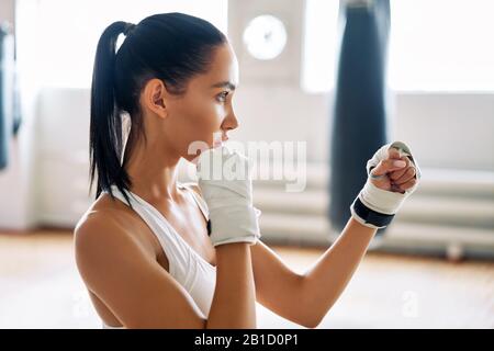 Giovane boxer donna che posa in combattimento posizione in palestra. Femmina sportiva pronta per la lotta Foto Stock