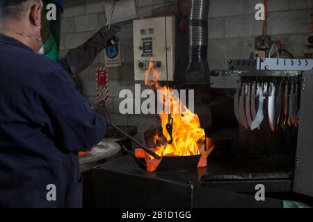 Processo di rinvenimento in fabbrica di coltelli. Forno, bagno d'olio e scarico Foto Stock