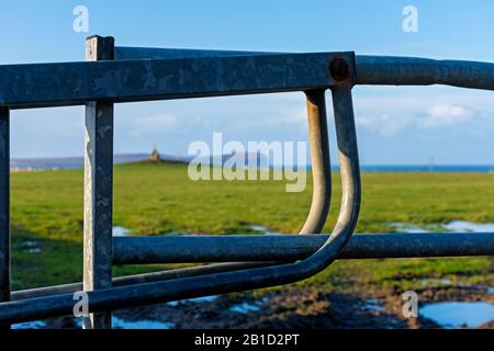 Dunnet Head e la croce di pietra sul Cairn di Mey, attraverso una porta fattoria vicino al villaggio di Mey, Caithness, Scozia, Regno Unito. Focalizzato sul cancello. Foto Stock