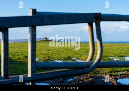 Dunnet Head e la croce di pietra sul Cairn di Mey, attraverso una porta fattoria vicino al villaggio di Mey, Caithness, Scozia, Regno Unito. Focalizzato sulla distanza. Foto Stock