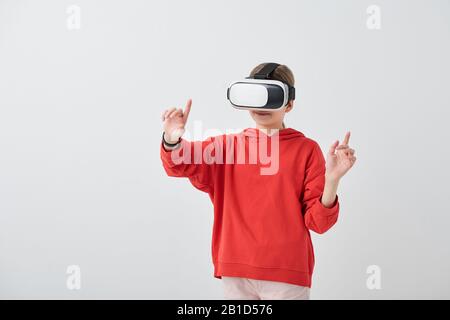 Content School girl in red hoodie gesturing mano mentre godendo la realtà virtuale in simulatore VR Foto Stock