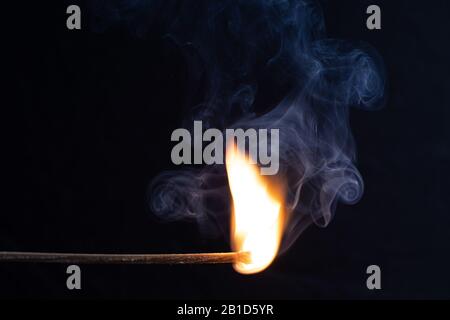 un fiammifero ardente con una fiamma brillante contro uno sfondo nero Foto Stock
