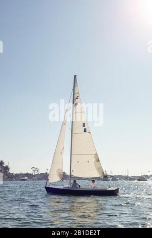 Le barche a vela scivolano sull'acqua a Newport Bay, Newport Beach, California, Stati Uniti. I nuovi marinai ricevono lezioni nella baia dove l'acqua è calma. Foto Stock