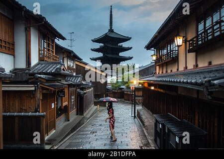 Una ragazza con un ombrello che indossa un abito colorato nella strada più panoramica di Kyoto, con la pagoda Yasaka sullo sfondo, Giappone Foto Stock