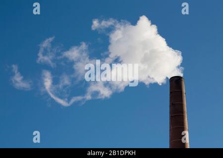 Pennacchi di fumo bianco che esce dai ciminiere contro i cieli soleggiati Foto Stock