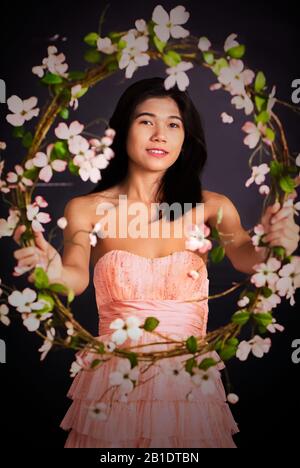 Sorridente ragazza teen biracial in abito satin tulle rosa senza spalline o abito da sole che tiene fuori una grande corona di fiori rosa Foto Stock
