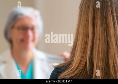 Giovane donna alla nomina dei medici. Vista dal retro. Il medico prescrive farmaci per il paziente. Personale medico che tiene le pillole in mano. Foto Stock