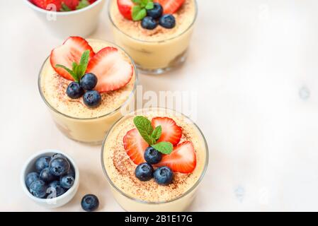In casa, squisiti dessert Tiramisu' in vetri decorati con fragola, mirtillo, menta bianca sul tavolo di legno, Foto Stock