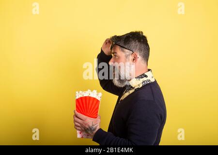 Bell'uomo con profilo fotocamera occhiali da sole che tengono una scatola piena di popcorn su sfondo giallo. Foto Stock