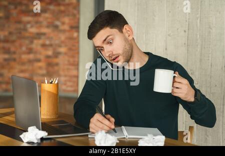 L'Uomo Sopraffatto Che Parla In Multitasking Sul Telefono Seduto In Ufficio Foto Stock