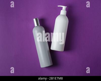 Shampoo grigio e balsamo bianco in bianco bottiglie cosmetiche su sfondo viola brillante Foto Stock