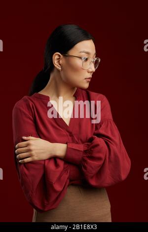 Girovita ritratto di donna asiatica indossando blusa rossa che posa rigido contro sfondo marrone in studio Foto Stock