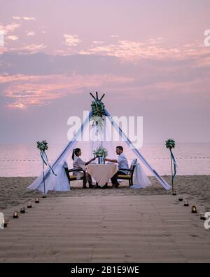 Giovane coppia Luna di Miele cena a lume di candela al tramonto sulla spiaggia, uomini e donne che cena sulla spiaggia romantica impostazione in Thailandia durante Foto Stock