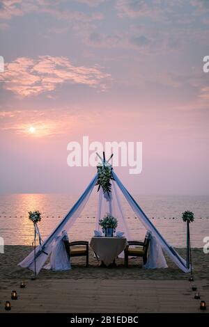 Giovane coppia Luna di Miele cena a lume di candela al tramonto sulla spiaggia, uomini e donne che cena sulla spiaggia romantica impostazione in Thailandia durante Foto Stock