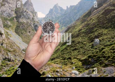 mano che tiene una bussola con uno sfondo dietro un paesaggio montuoso Foto Stock