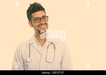 Studio shot di giovani felici persiano medico uomo sorridente e pensando indossando occhiali da vista Foto Stock