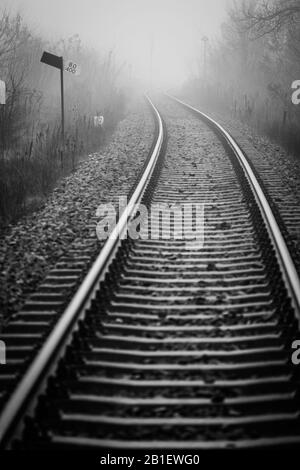 Prospettiva della pista ferroviaria scomparendo in nebbia mattina nebbia - immagine monocromatica Foto Stock