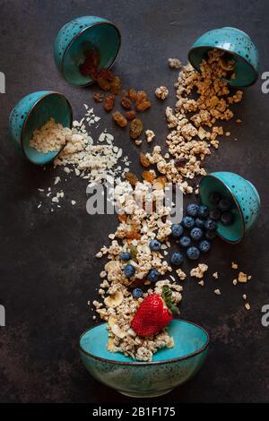 Granola, mandorle, uva passa e mirtilli - gli ingredienti per una sana colazione. Primo piano, vista dall'alto su sfondo scuro. Foto Stock