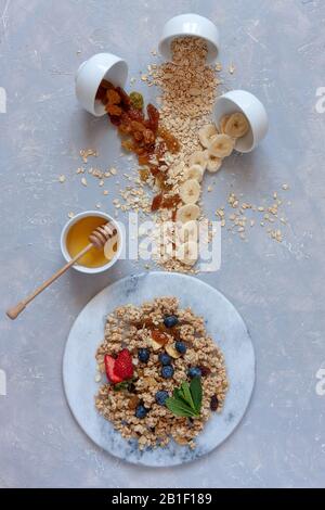 Granola, mandorle, uva passa, latte, miele e mirtilli - gli ingredienti per una sana colazione. Primo piano, vista dall'alto su sfondo chiaro. Foto Stock