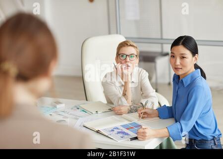 Tre giovani donne moderne che discutono il progetto in riunione di affari Foto Stock