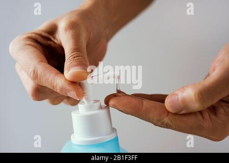 ostruzione di un uomo caucasico che desinfetta le mani con igienizzatore per le mani da una bottiglia blu Foto Stock