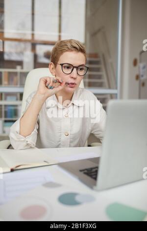 Ritratto di moderna donna d'affari che usa il laptop mentre si collega in rete in ufficio Foto Stock