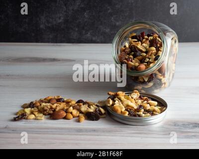 Dadi, semi e frutta secca che fuoriesce da un vaso di vetro trasparente nel coperchio e sul tavolo! Sano, nutriente imballato buoni carbs e buon snac grasso Foto Stock