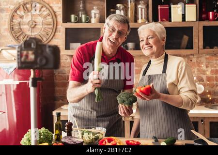 Gioiosa Senior Couple Cooking A Camera, Registrazione Video Culinario In Cucina Foto Stock
