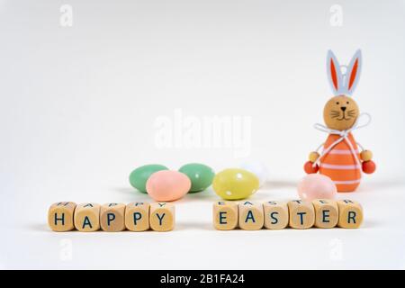 Blocchi di legno con lettere che dicono 'buona Pasqua' di fronte a colorate uova di pasqua e un coniglietto di pasqua su sfondo bianco con spazio copia Foto Stock