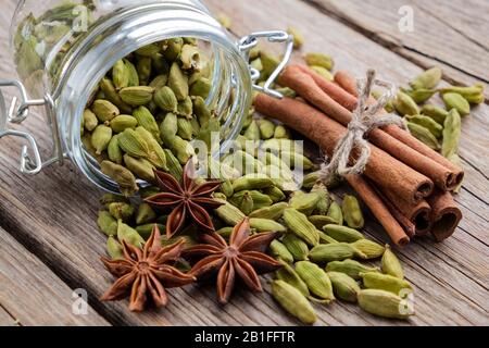 Vaso di interi baccelli di cardamomo. Bastoncini di cannella, semi di cardamomo e stelle anice sul tavolo. Foto Stock