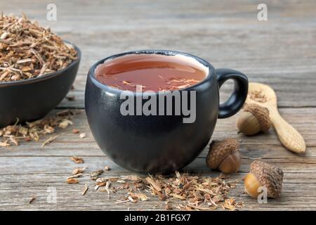 tazza da tè alle erbe, sana corteccia di quercia in recipiente di ceramica nera e acorns su tavolo di legno. Medicina di erbe. Foto Stock