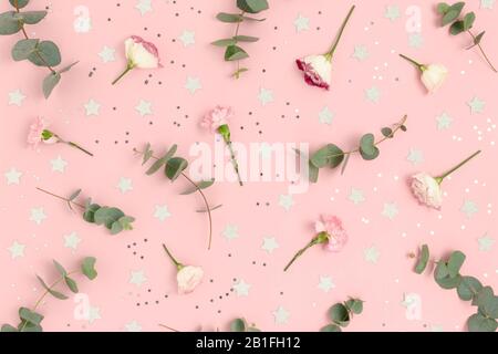 Modello realizzato in eucalipto, eustoma, fiori di garofano e stelle confetti. Concetto di vacanza su sfondo pastello rosa. Foto Stock