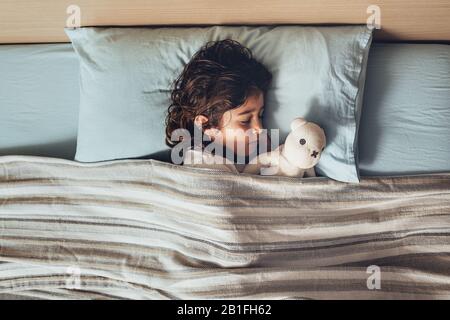 vista dall'alto di una adorabile bambina che dorme a letto abbracciando il suo orsacchiotto, infanzia felice e sano concetto di riposo Foto Stock